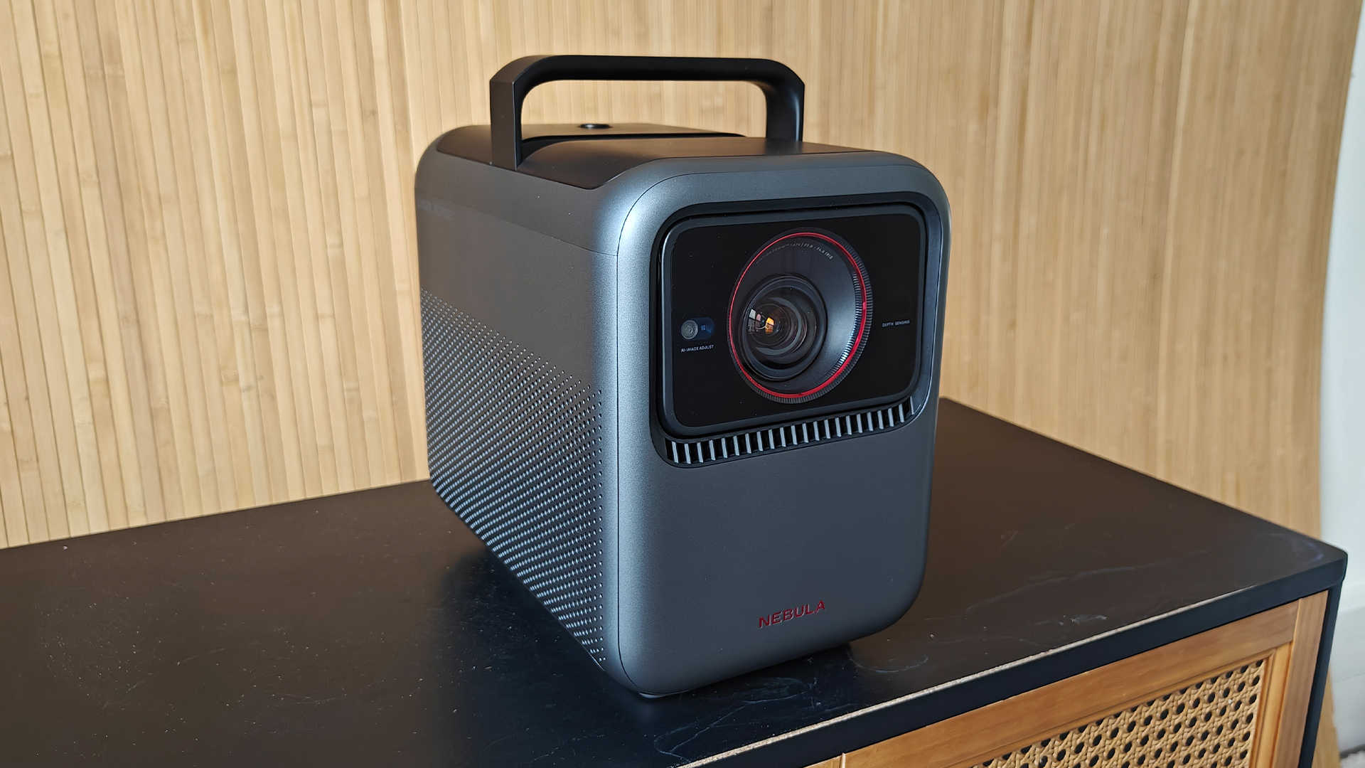 Nebula X1 home cinema projector on black wooden surface against wood wall