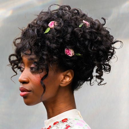 A woman with a curly updo with flowers decorated throughout it. 