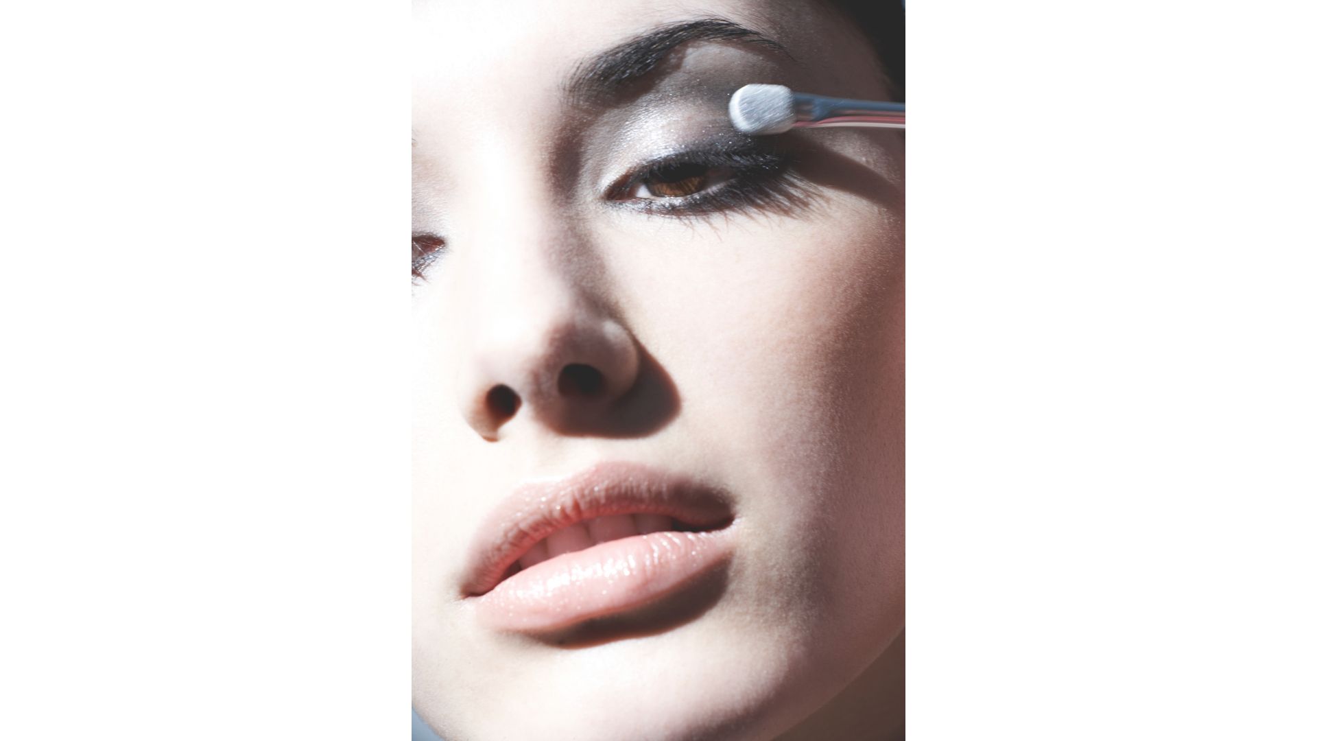 A woman applying eyeshadow onto a smoky eye look on a blue backdrop