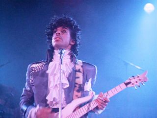 prince in a purple suit with a white frilly shirt holding a guitar on stage in Purple Rain