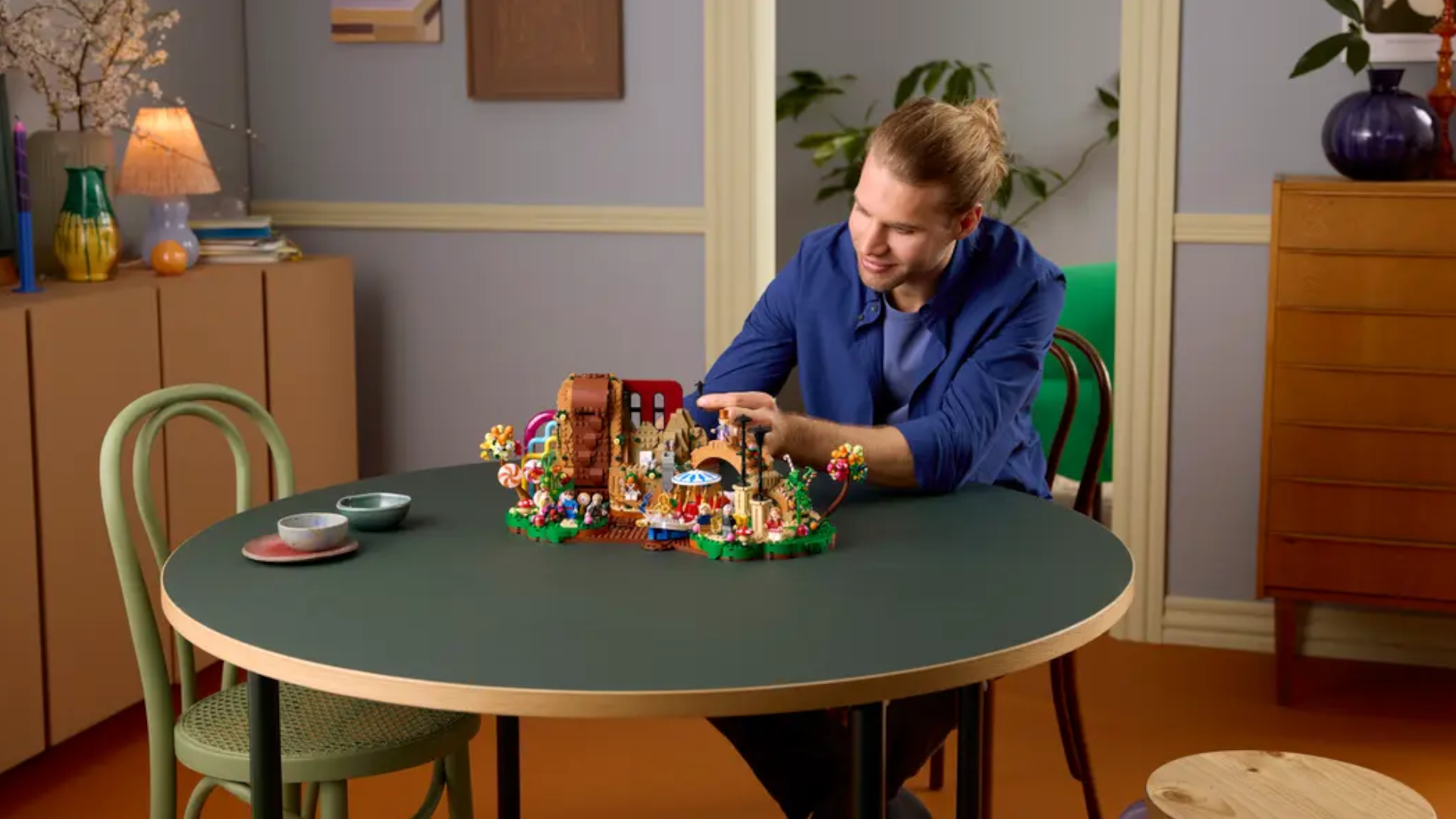 A man sitting at a table smiles while looking down at the Lego Willy Wonka &amp;amp; the Chocolate Factory set which is laid out in front of him