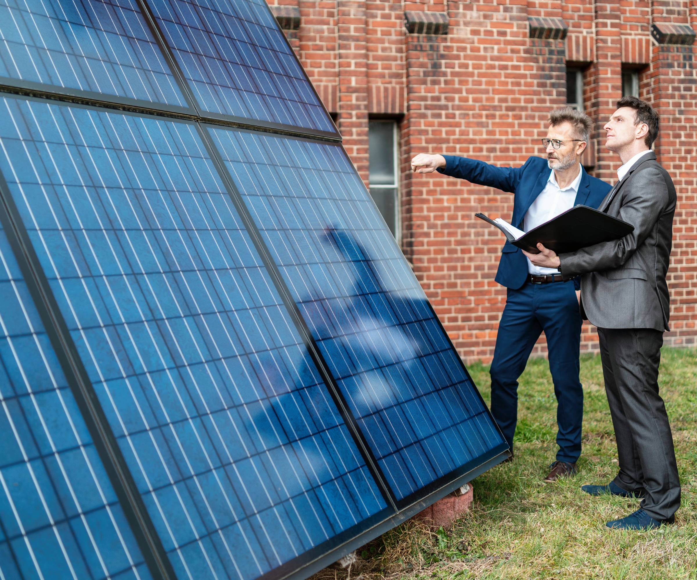 two men in suits stood looking and pointing at ground mounted solar panels