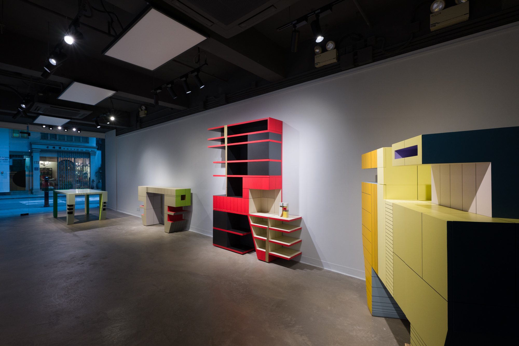 A modernist design exhibition of colorful furniture pieces installed in a gallery on the cusp of night.