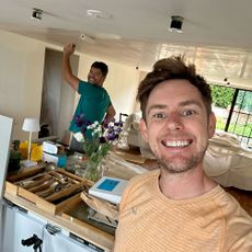 Two men in kitchen, one taking selfie, one painting the ceiling