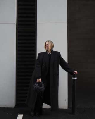 Woman wears black coat, black top, black trousers and black bag