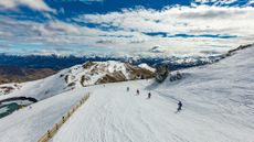 Skiers go down a slope on a bright but cloudy day at the Coronet Ski Resort in Queenstown, New Zealand