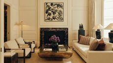 Modern luxury living room featuring a cream sofa, two armchairs, dark marble fireplace, abstract black-and-white wall art, and purple flowers on a coffee table