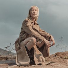 Blonde woman wearing trench coat in desert with grey sky
