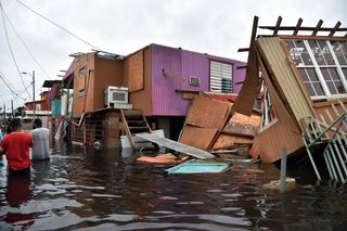 People walk in a flooded street next to damaged houses in Juana Matos, Catano, Puerto Rico, on Sept. 21, 2017.