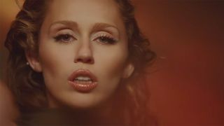 Miley Cyrus staring at the camera with makeup on in the new music video for something beautiful, headshot-style.