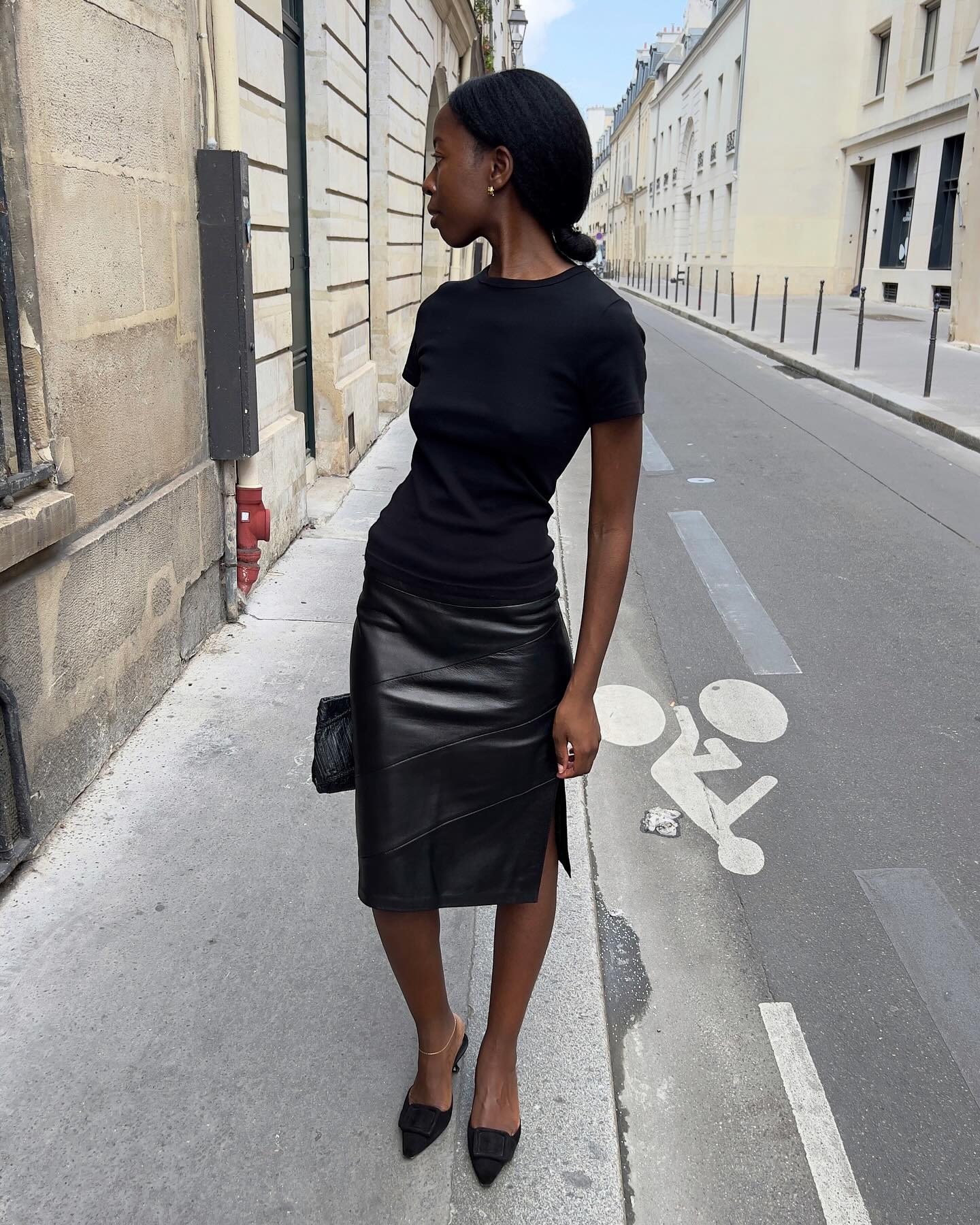 Sylvie Mus wearing a black T-shirt, a leather pencil skirt, and Manolo Blahnik mules.