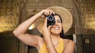 A person in a hat and a yellow dress holding a Canon EOS R10
