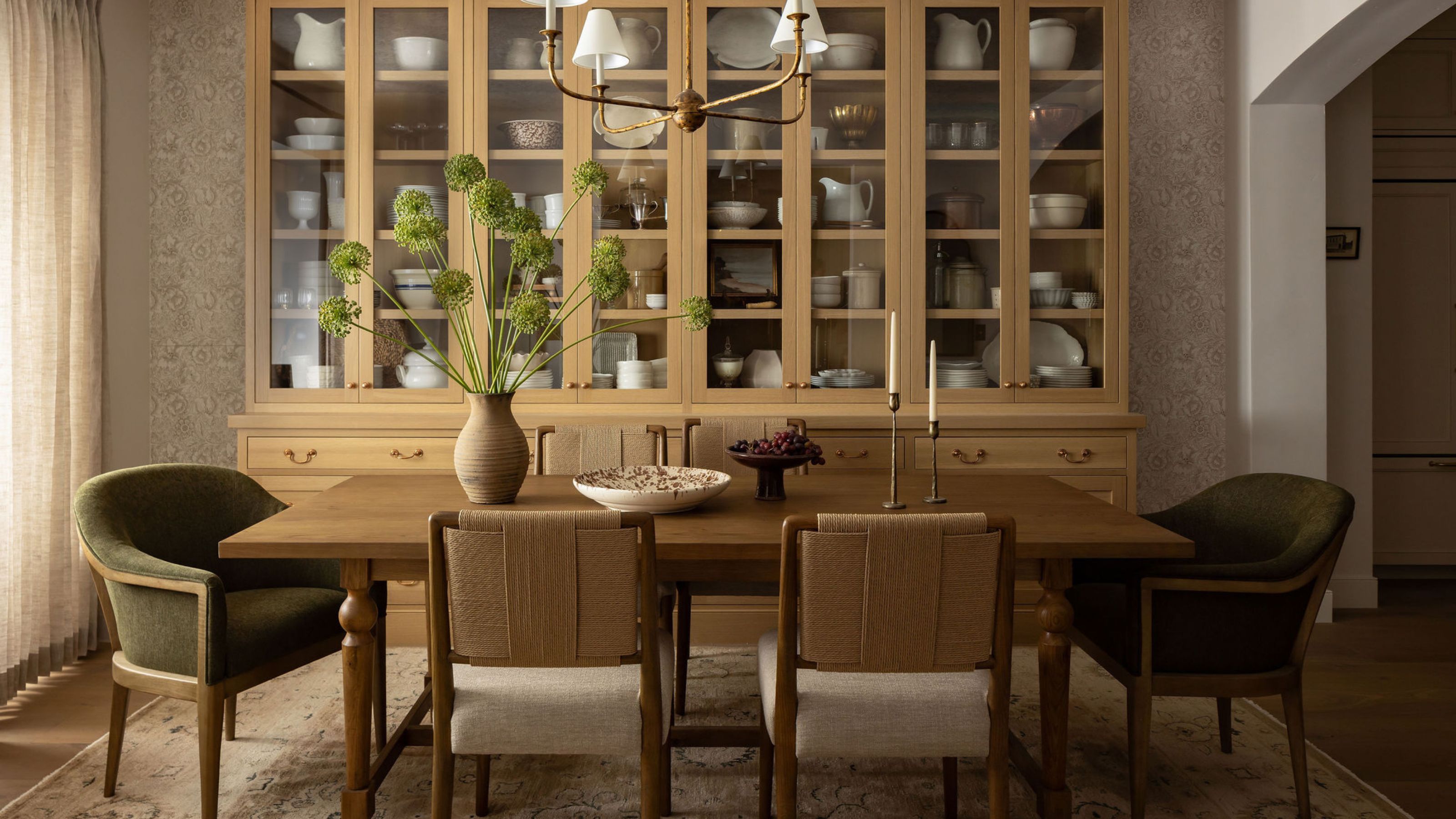 a layered dining room with large oak storage, wooden dining table, mis matched chairs, rug and pendant light