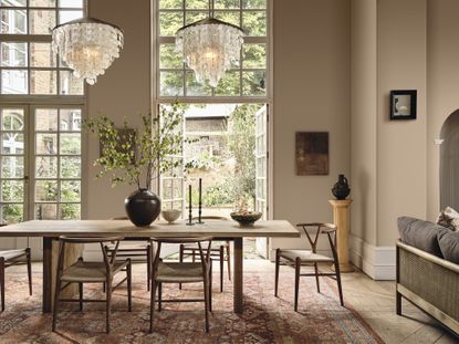 A dining room painted in a warm beige with a wooden dining set, Persian rug and large French windows 