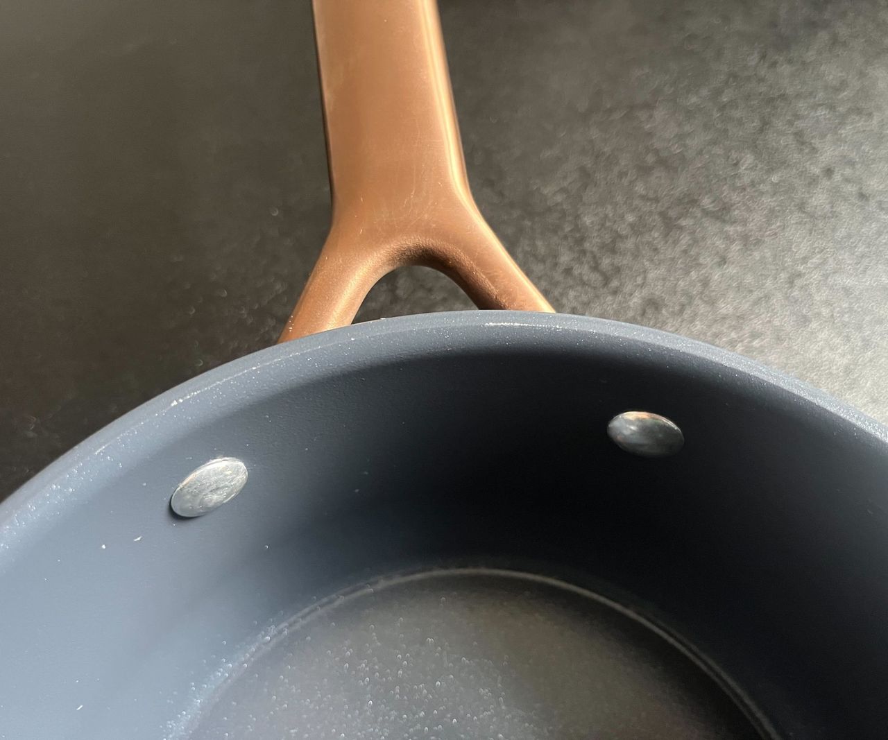 Slight peeling on the edge of a blue pan with a copper handle, on a black kitchen counter