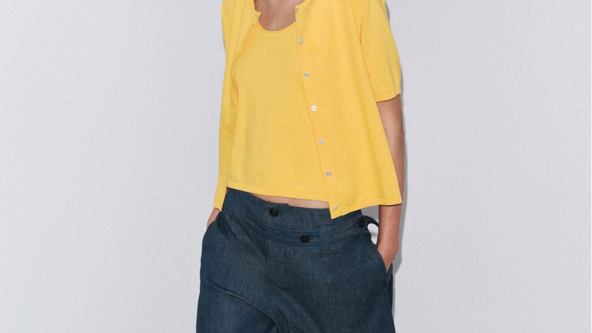 Woman wearing a short-sleeve yellow cardigan and matching top with jeans.