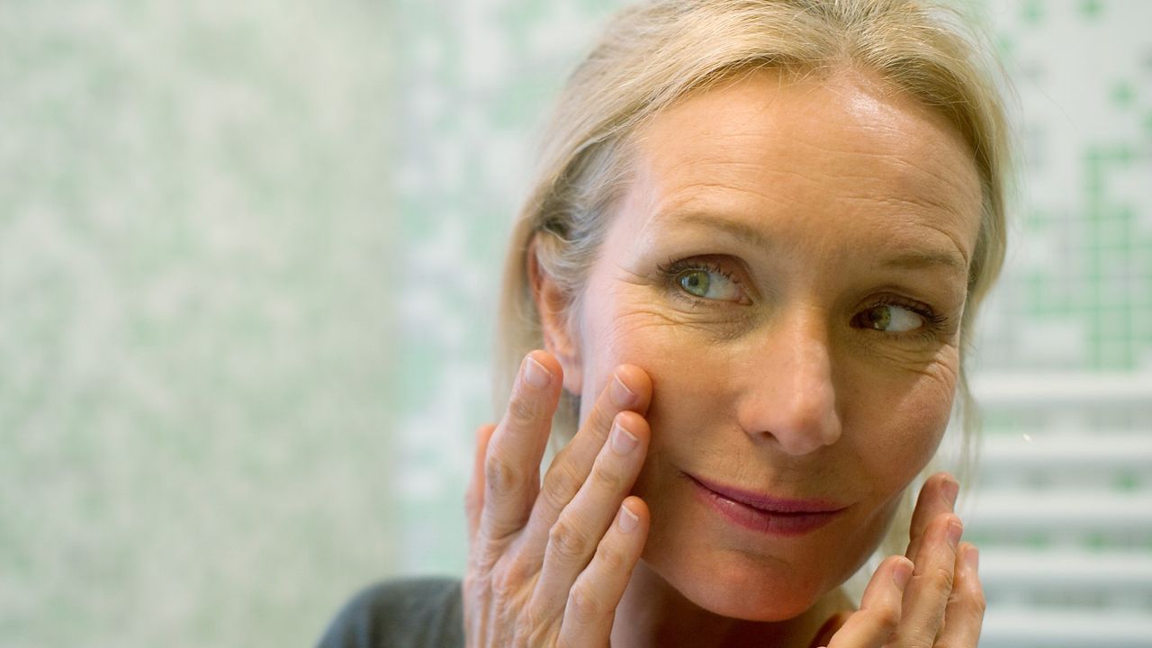 Mature woman looking at reflection in mirror with hand on cheek - stock photo