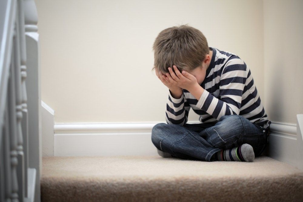 Upset problem child with head in hands sitting on staircase.