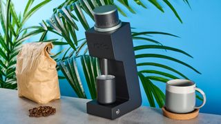 The Varia VS3 coffee grinder in use on a stone surface with a blue background