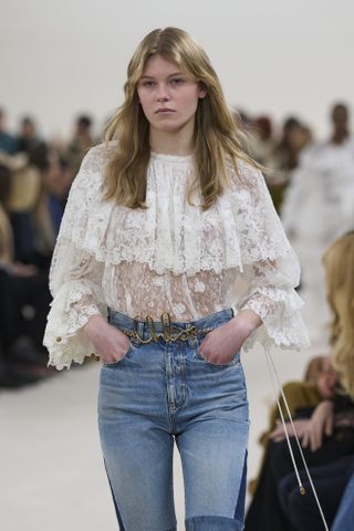 Woman on runway in white lace blouse.