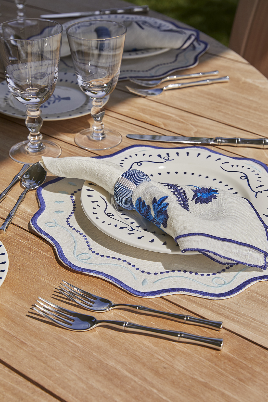 A summery blue and white table setting, with charger, plate, and napkin, sits outside on a wooden table.