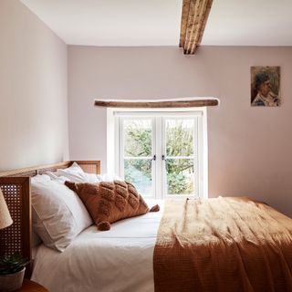 cosy pink bedroom with wooden beams and copper tone bedding and rattan headboard