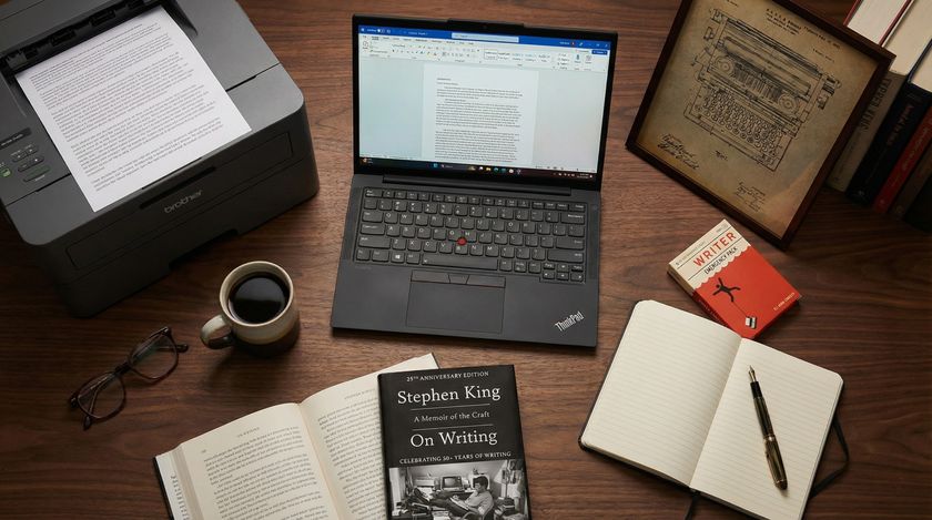 A laptop, printer, notebook, and books on a writing desk