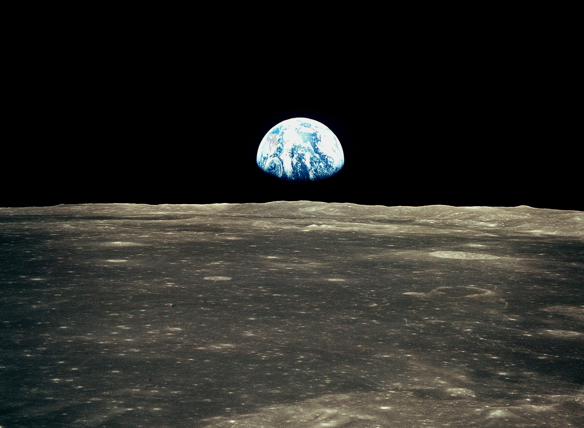 This view from the Apollo 11 spacecraft in July 1969 shows the Earth rising above the moon&#039;s horizon. The lunar terrain pictured is in the area of Smyth&#039;s Sea on the nearside.