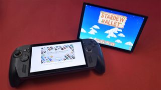 A handheld gaming device with a large screen and controls on each side rests on a pink surface. 