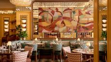 A huge mirror painted in abstract pastel shapes overlooks the green and pink upholstered seating area of the Cicchetti Piccadilly restaurant