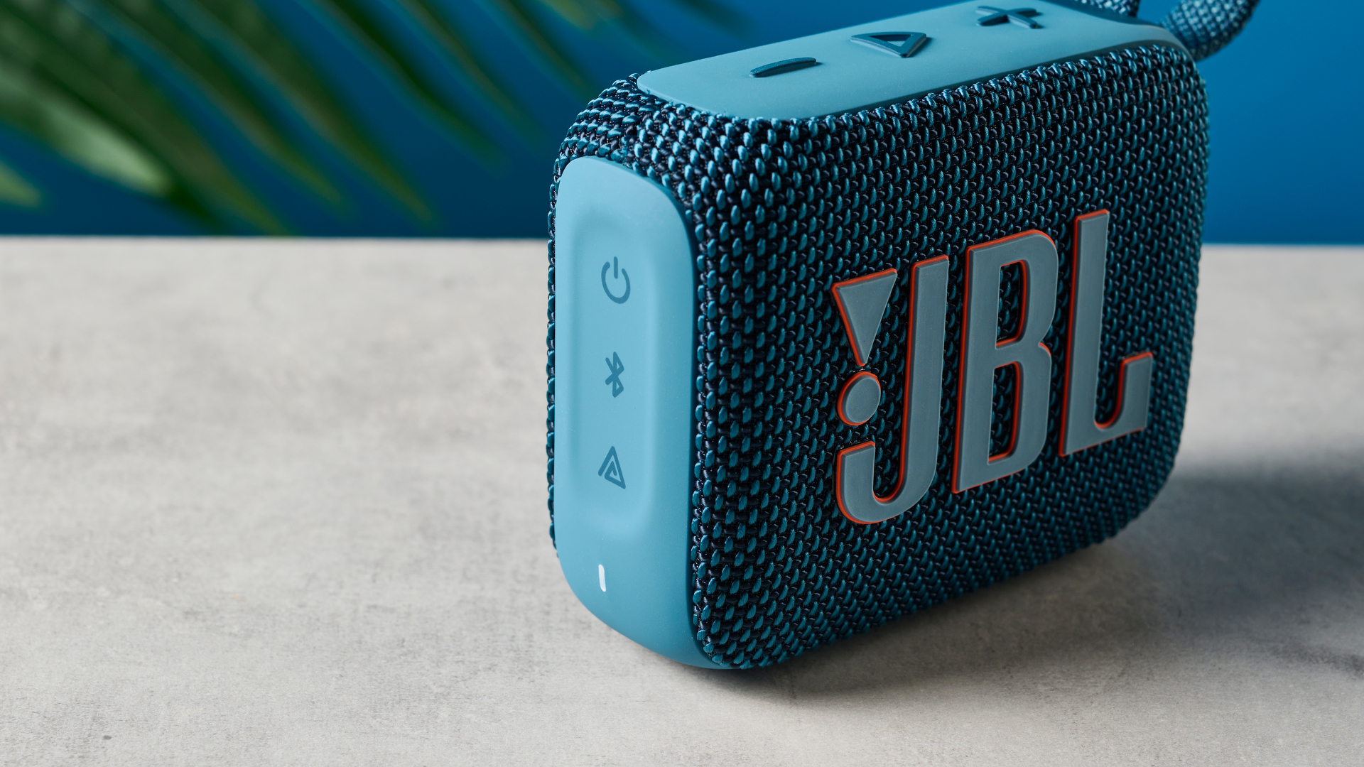 A photo of the JBL Go 4 in blue on a concrete surface against a blue wall.