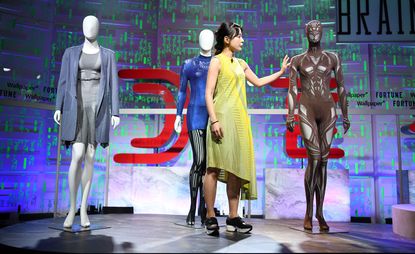 Tamae Hirokawa on stage presenting three mannequins with body knit suits. 