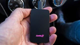 Holding Carlinkit 5.0 adapter with logo flashing pink.