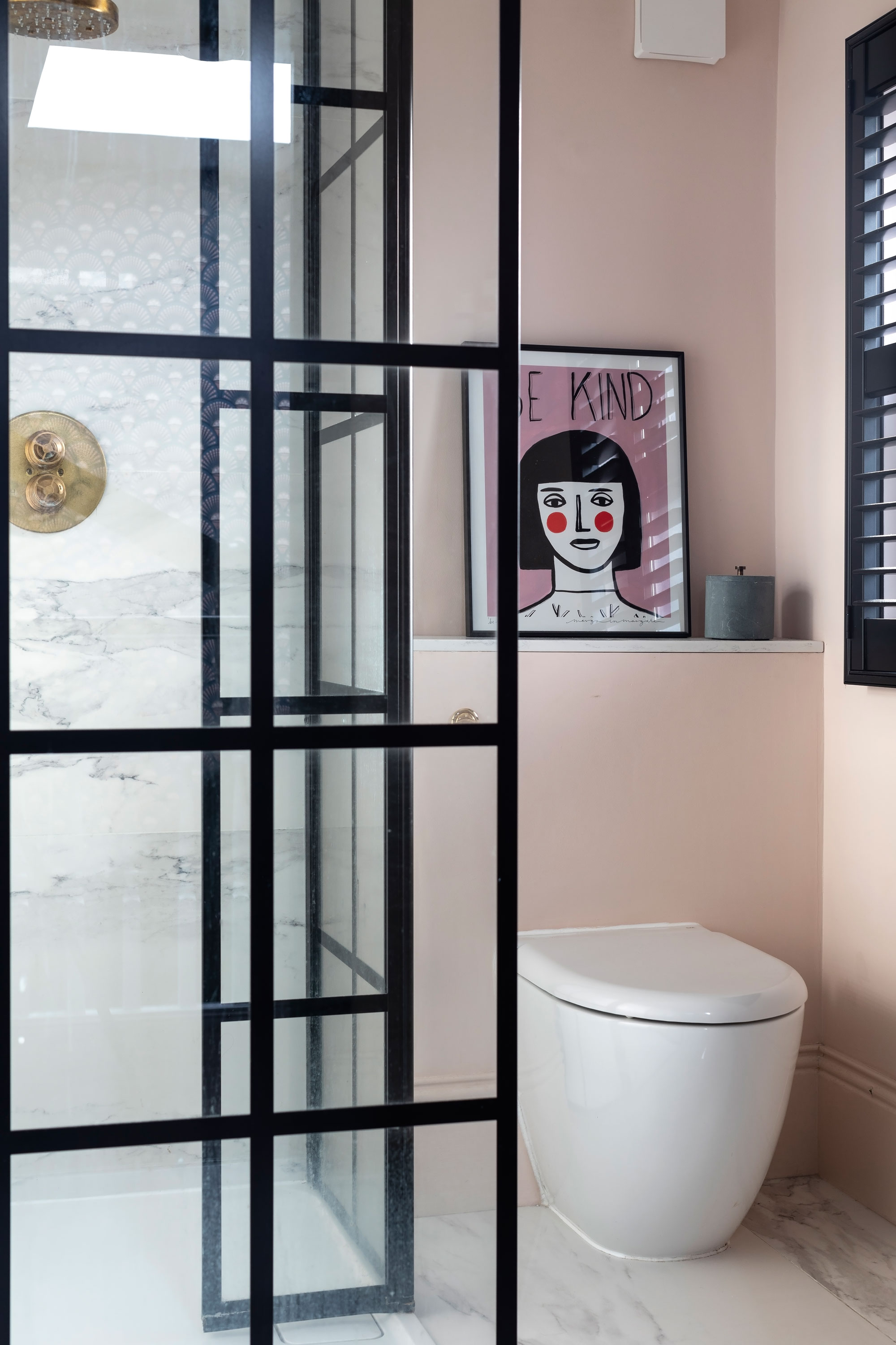 A pink bathroom idea with white toilet, black framed shower and framed art on shelf