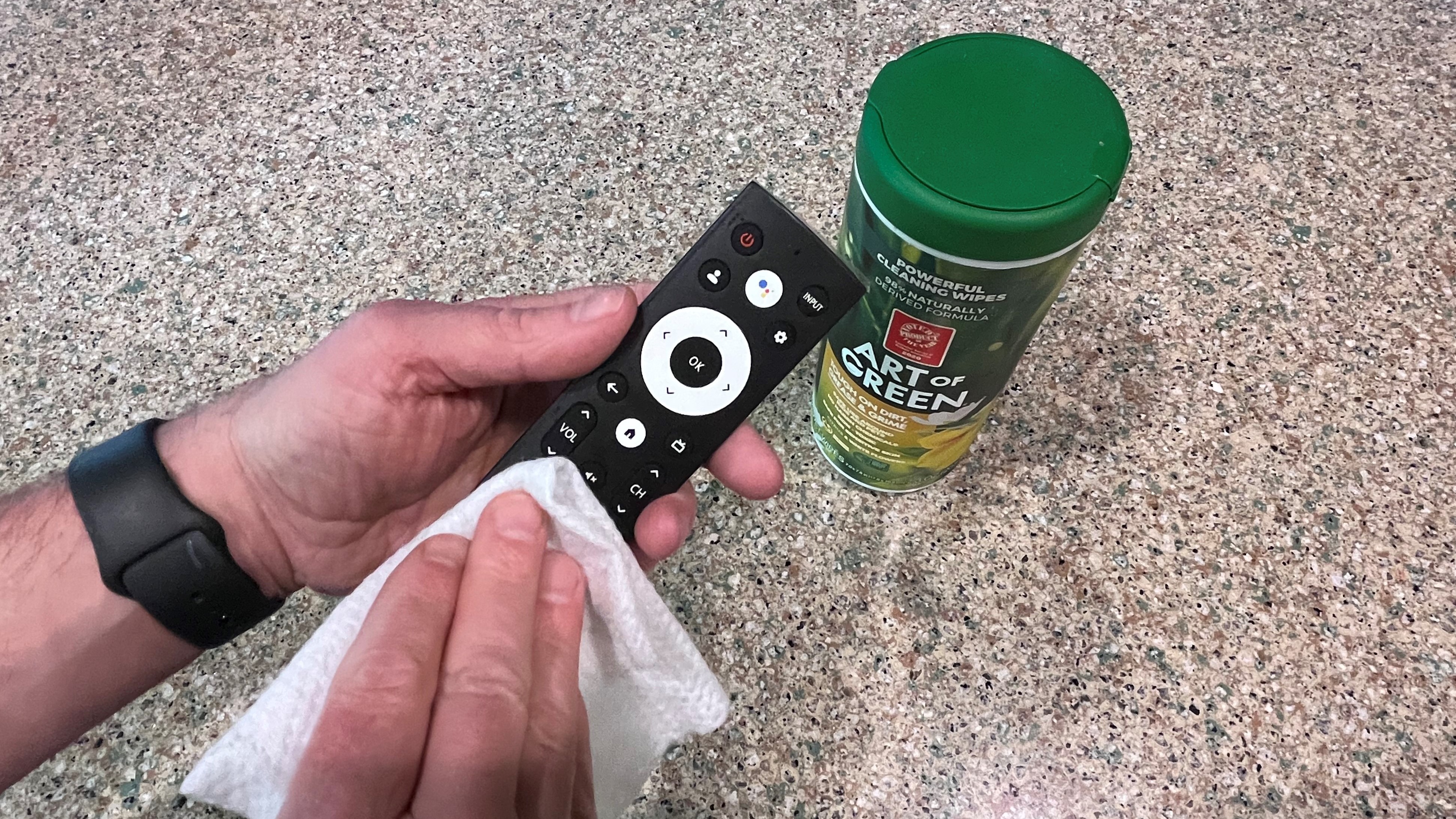 hand wiping remote control to clean it with wipes container in background