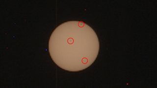 An image of the sun with three large sunspots circles by a red ring
