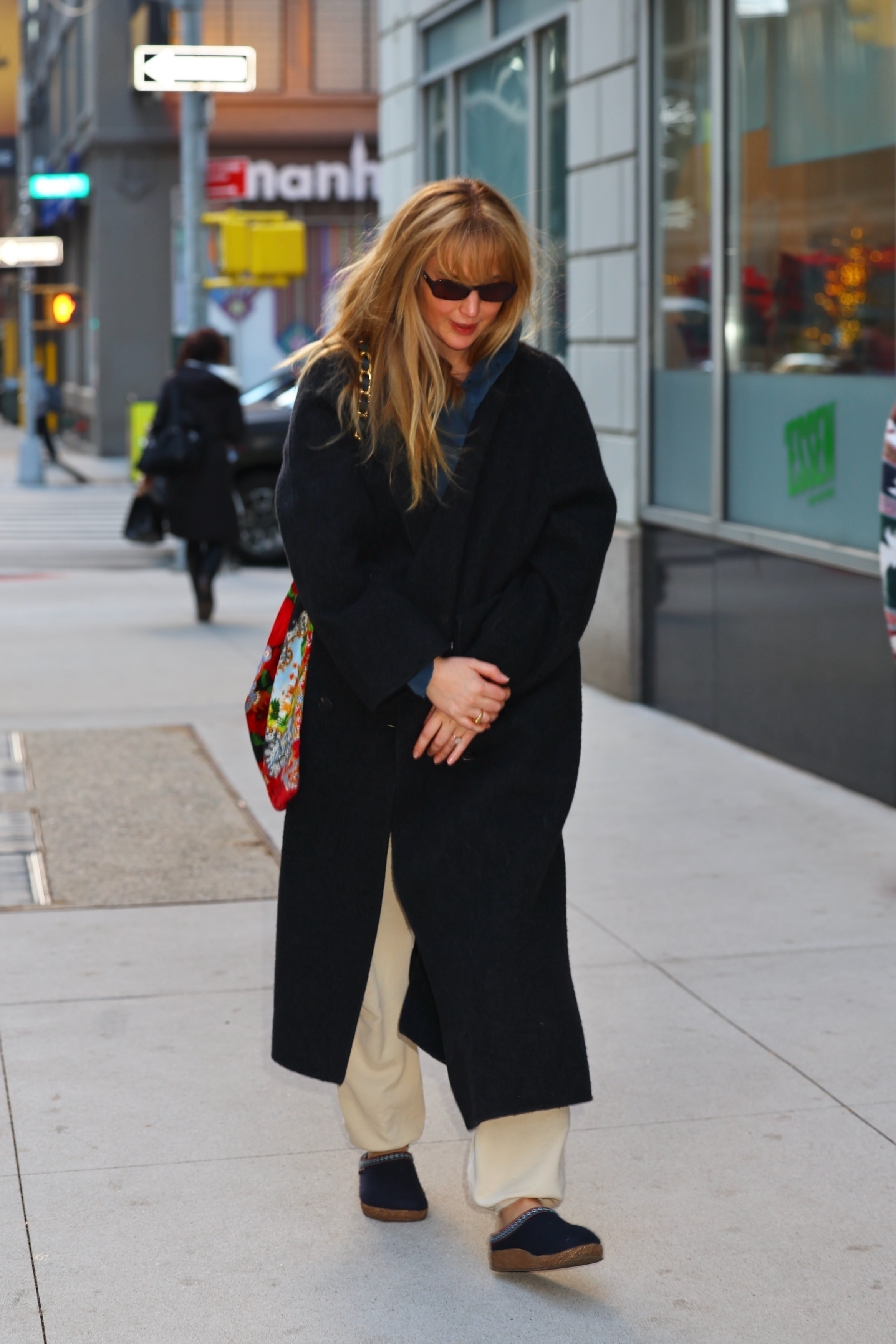 Jennifer Lawrence walks down the street in New York wearing navy felted shoes, cream trousers and a black coat.