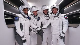 Four Crew-8 astronauts in white SpaceX spacesuits with their arms together for ahead of launch.