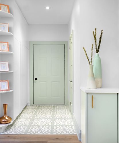 Mint green front door at end of white entryway with small cabinet and tiled floors