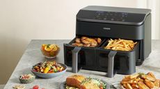 COSORI dual basket air fryer with prepared food including fries, chicken wings, and salmon