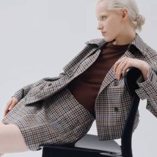 A model wearing a plaid skirt and a matching jacket with a brown top from Neiman Marcus. 