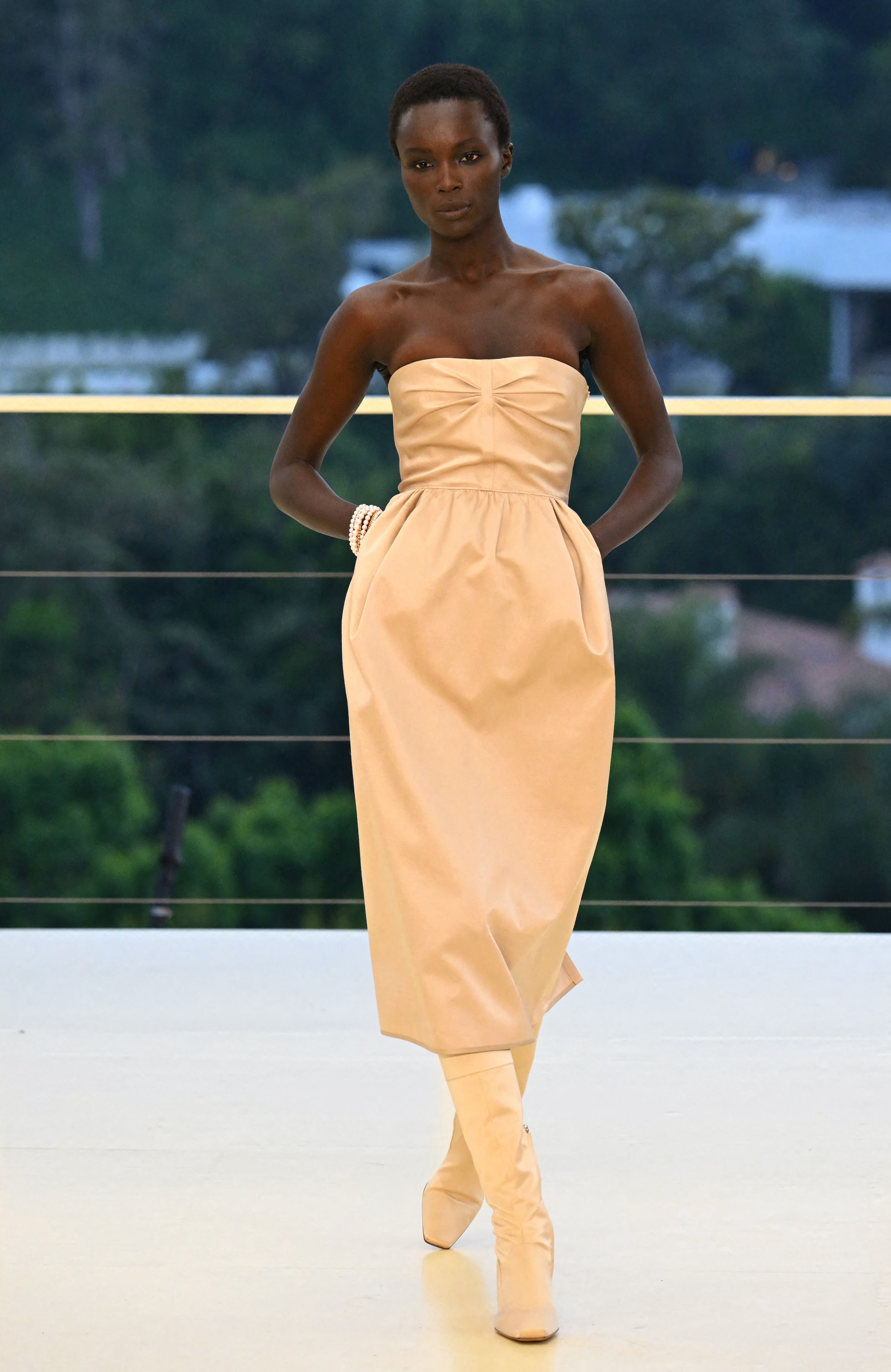 a woman wears a dress and boots at the hermes cruise 2027 show.
