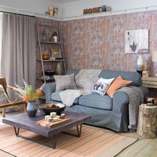 Living room with pink and orange woodland wallpaper, a complimenting orange rug, a blue couch with cushions and a grey slab coffee table