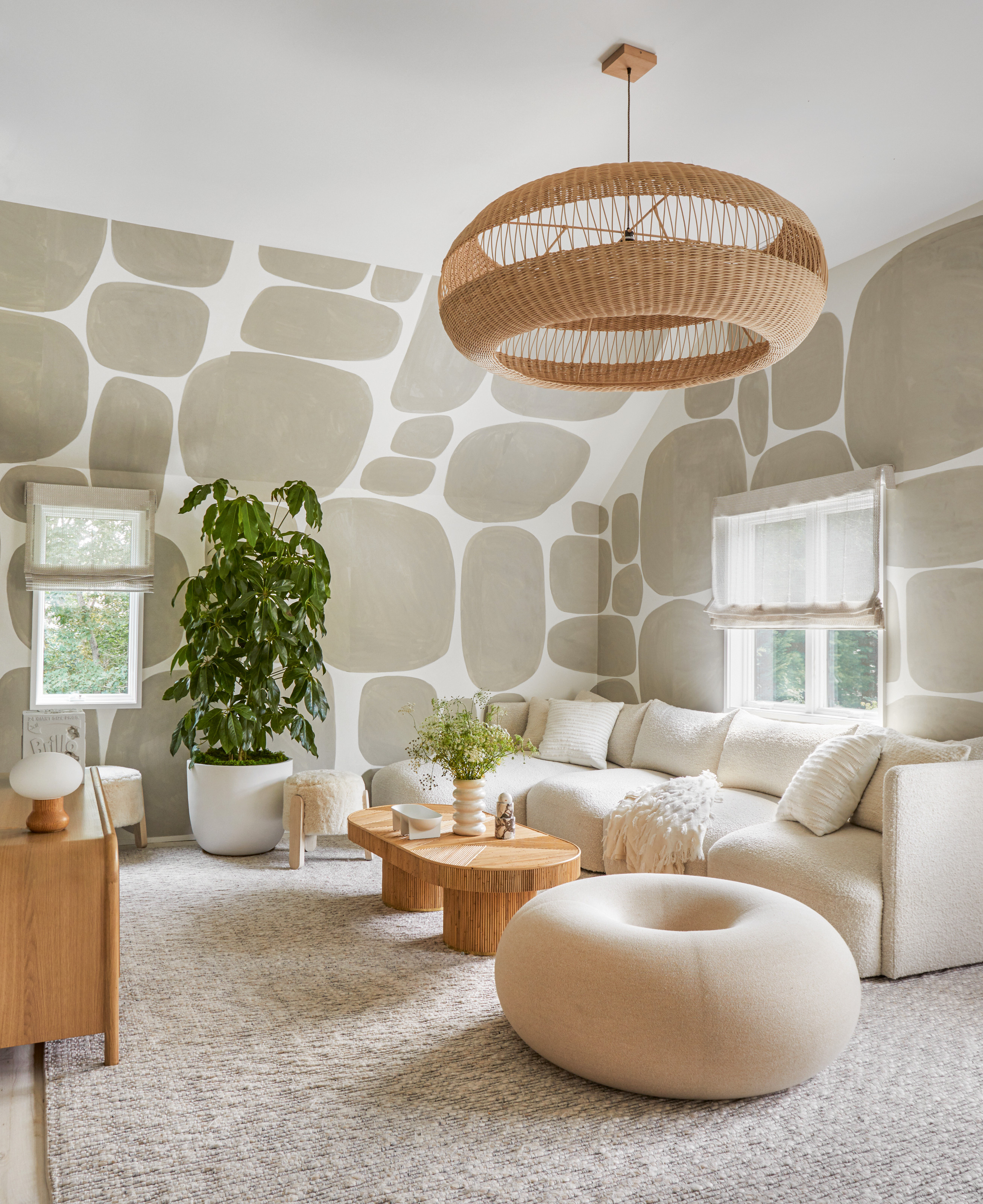 Snug with abstract pattern beige wallpaper, white sofa, white donut pouffe and rattan pendant light