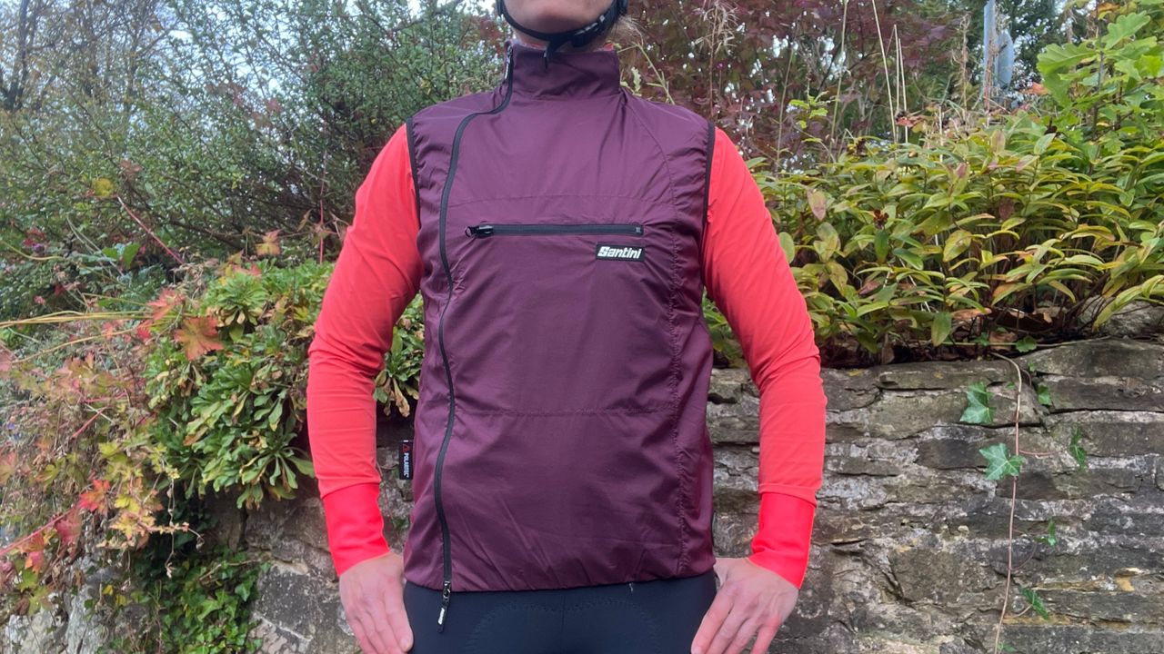 The purple Santini Alpha Pack Vest warn with a pink jacket underneath in front of a stone wall