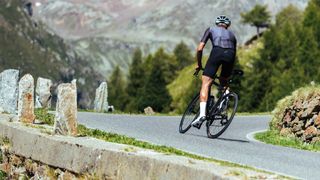 A white male road cyclist is out of the saddle and sprinting up a mountain road