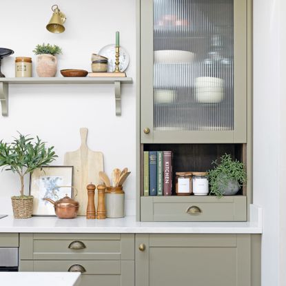 olive green kitchen cabinets with white worktop holding an assortment of items