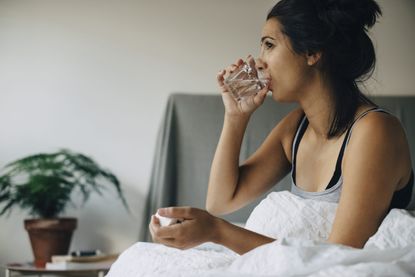 Woman taking medicine while sitting on bed at home