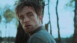 Robert Pattinson looks behind him in Die My Love, a look of horror and blood on his face.