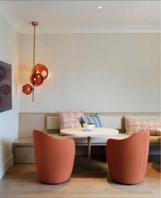 Dining area with greige banquet seating, two terracotta armchairs, terracotta ceiling light, terracotta cushion and light blue cushion
